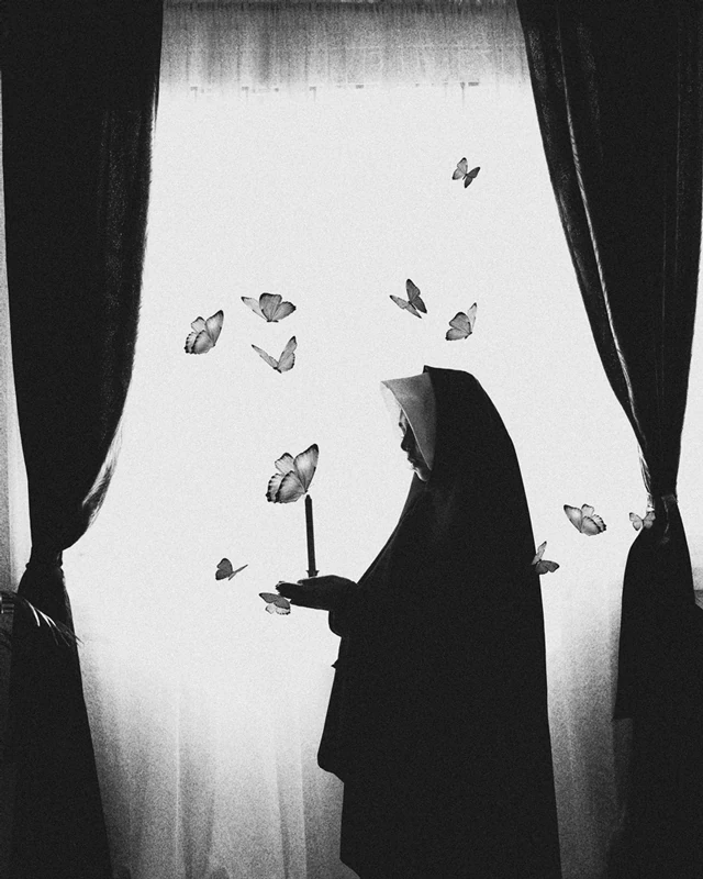 Black and white photograph of a nun in front of a giant window, holding a candle, surrounded by butterflies.