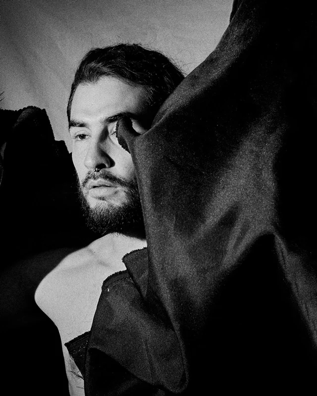 Black and white photograph of a man coming out of some canvases that are in the air.