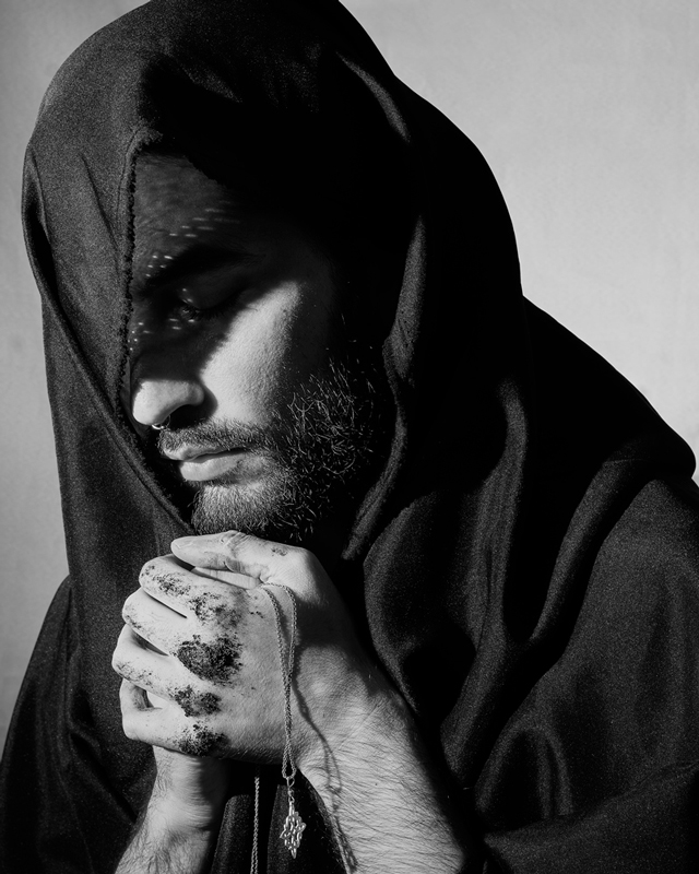 Black and white photograph of a man praying with a robe on his face and a chain in his hands.