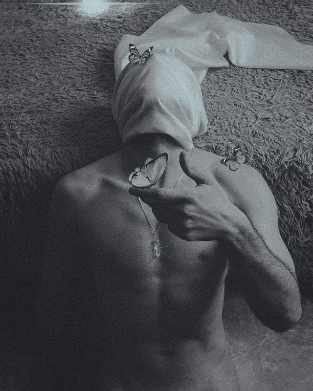 Black and white photograph of man with butterflies on hands and head.