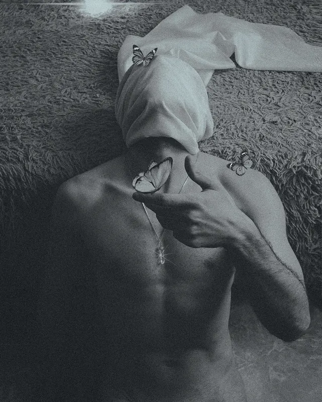 Black and white photograph of man with butterflies on hands and head.