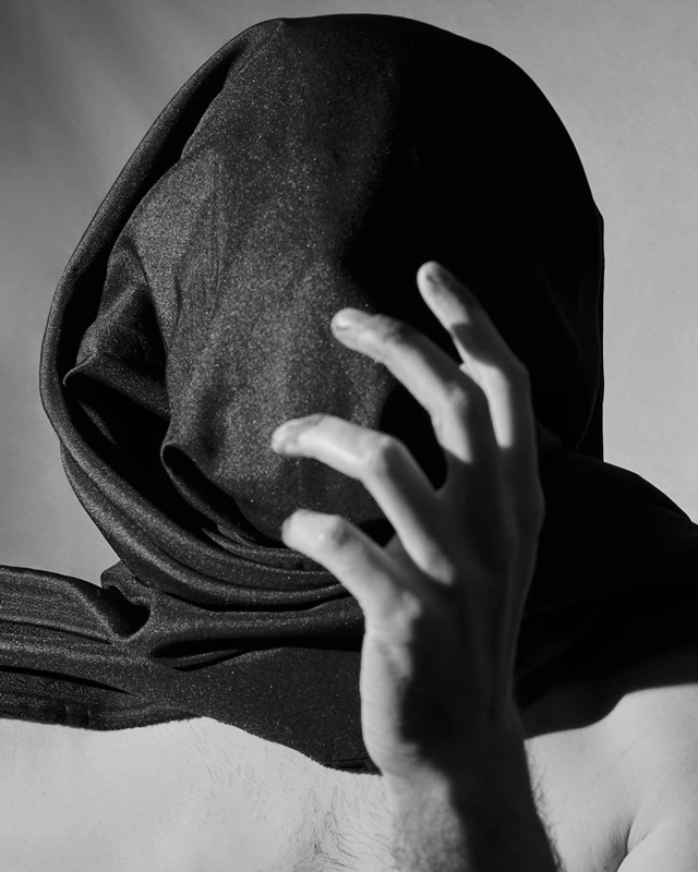 Black and white photograph of a man with his face completely covered by a blanket.