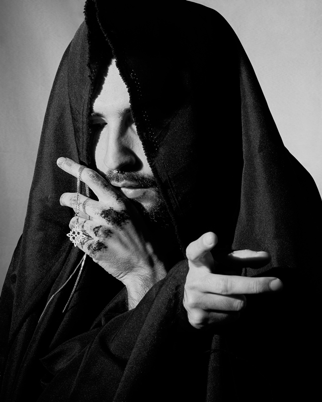 Black and white photograph of man with tunic on his face and a chain in his hand.