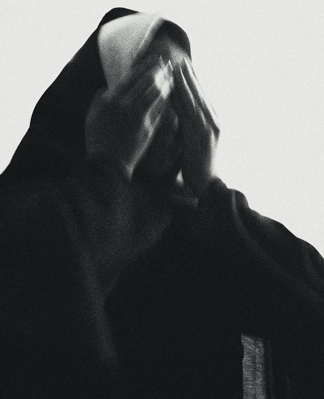 Black and white photograph of a nun covering her face with her hands.
