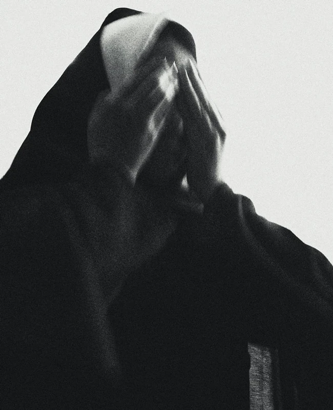 Black and white photograph of a nun covering her face with her hands.