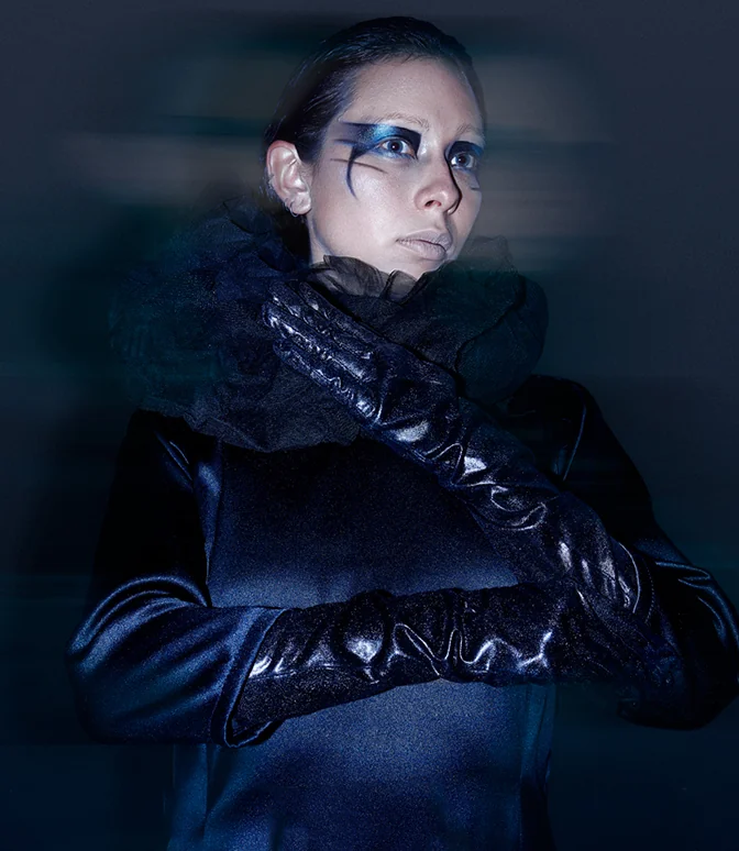 Fotografía editorial de fondo azul oscuro, mujer con maquillaje azul y guantes de cuero
