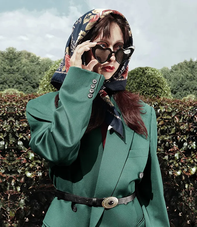 Fotografía editorial de mujer con saco verde y gafas en forma de corazón