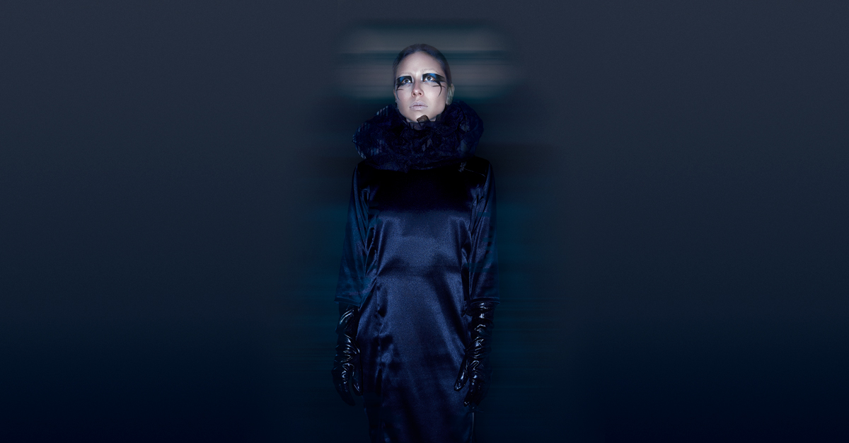 Portada editorial mujer con traje largo de color azul, guantes negros y maquillaje artístico azul oscuro, mirando al infinito