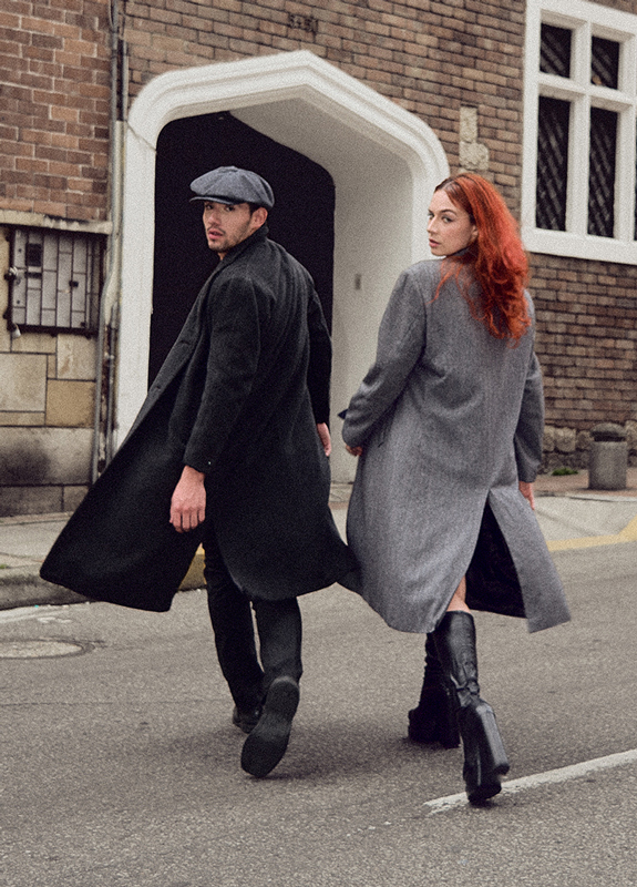 Portada editorial una pareja de hombre y mujer de espaldas, con gabanes largos, girando para mirar a la cámara