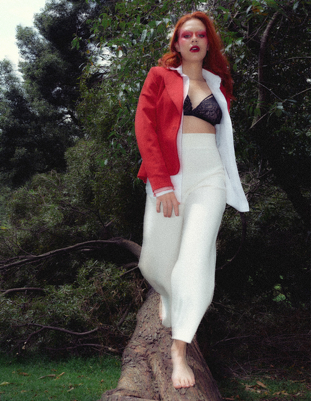 Portada editorial mujer con saco rojo y pantalón blanco, caminando arriba de un tronco de árbol caído
