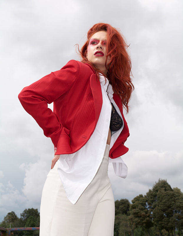 Portada editorial mujer con saco rojo y pantalón blanco, mirando al horizonte.