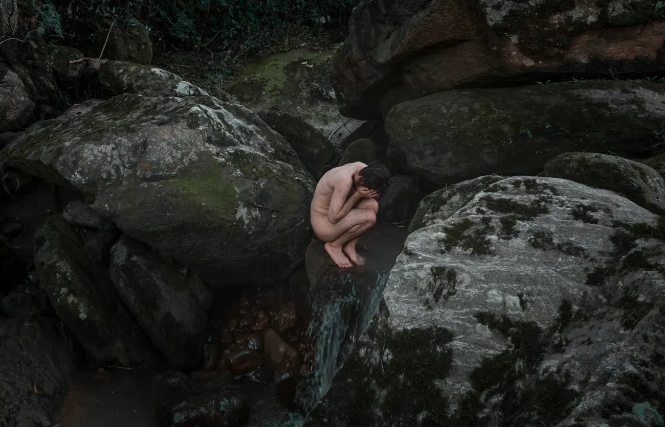 Hombre sentado en una cascada con las manos tapando su rostro
