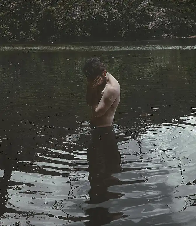 Hombre en medio de un lago, con las manos en el rostro