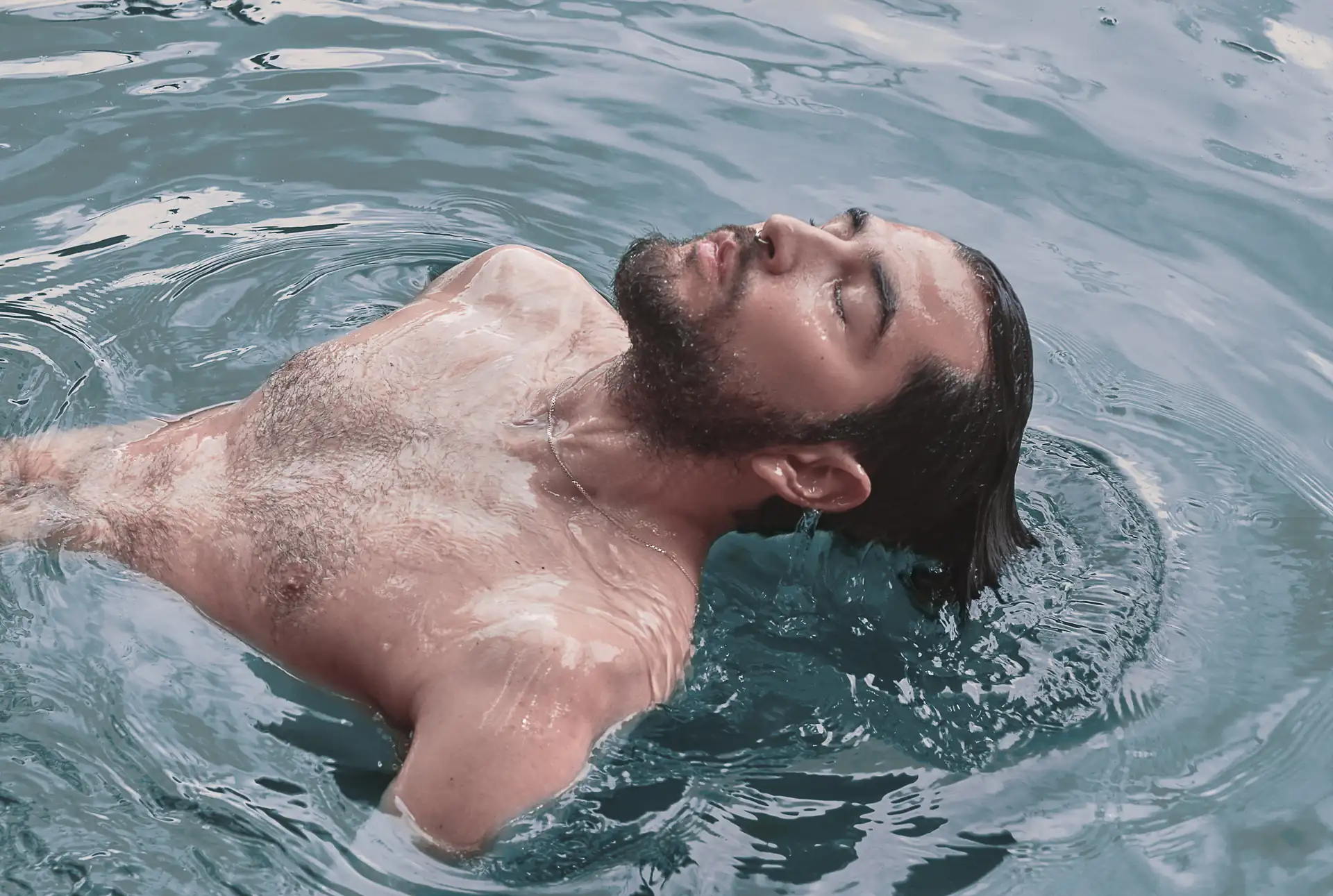 Hombre sacando su rostro en medio de un lago, con los ojos cerrados