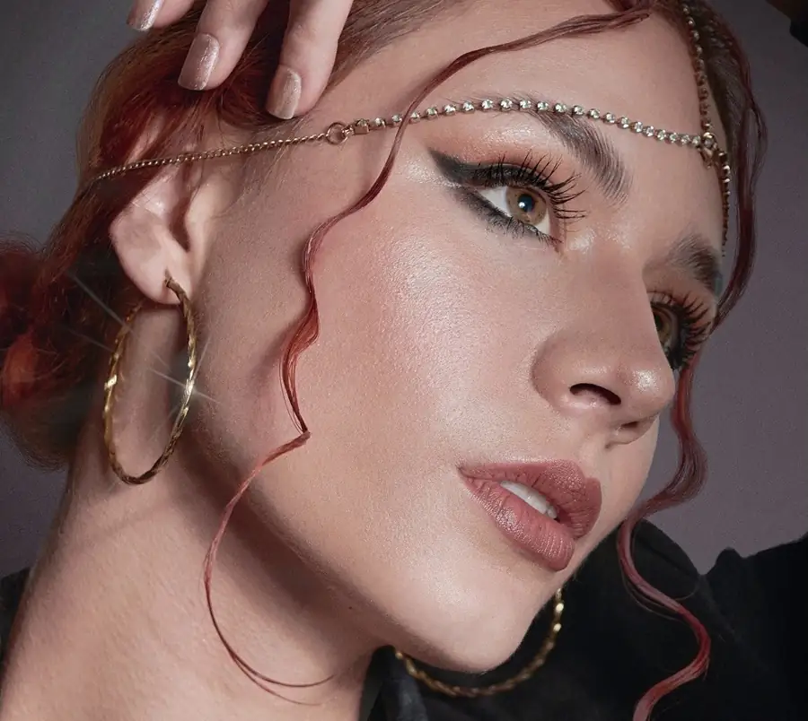 Beauty photograph of a woman gazing at the horizon, wearing a chain on her forehead and gold earrings.