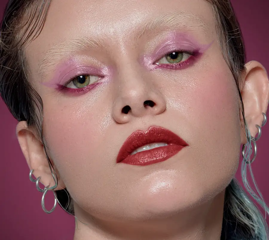 Beauty photograph of a woman with white skin and green eyes, with a magenta background