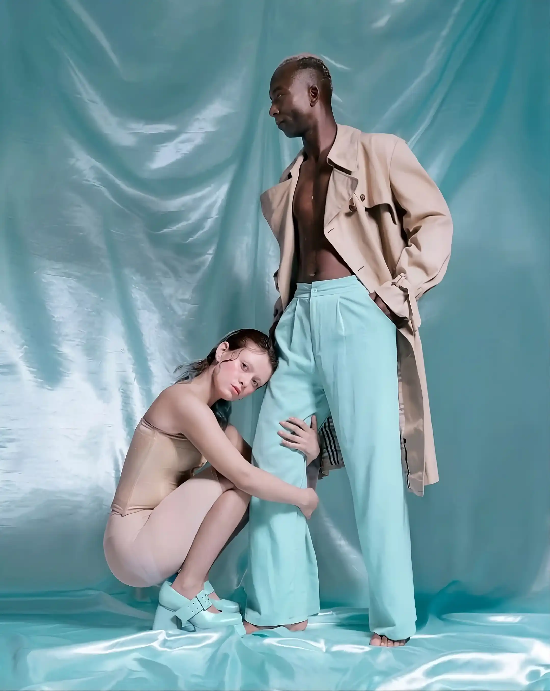 Fotografía editorial, de una mujer de rodillas, abrazando el piel de un hombre que esta de pie, vestido con un gabán mirando el horizonte
