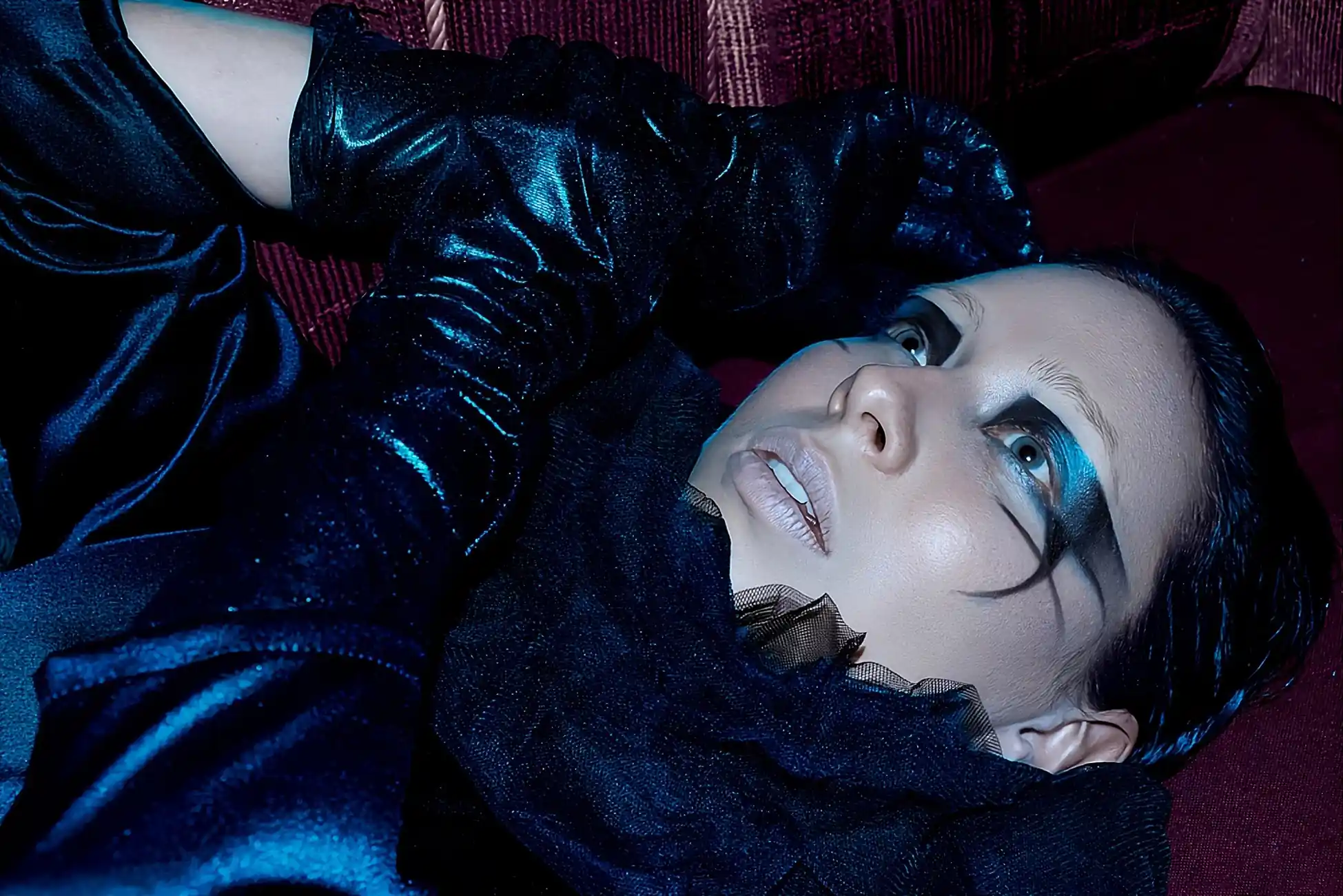 Fotografía editorial de mujer de ojos azules y piel blanca, acostada en un sofa, en primer plano, mirando hacia arriba