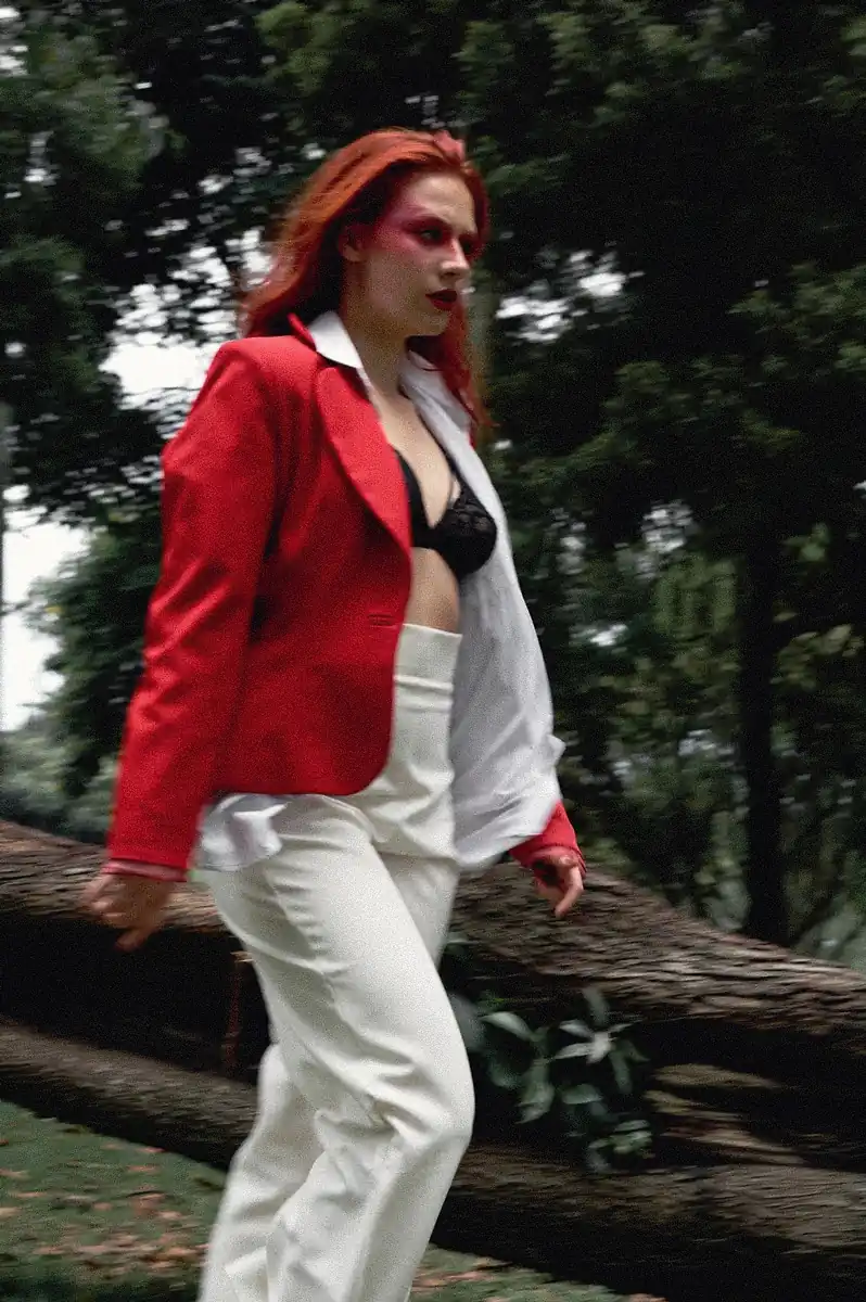 Fotografía editorial d euna mujer corriendo por el bosque, vestida con una saco rojo y pantalones beige