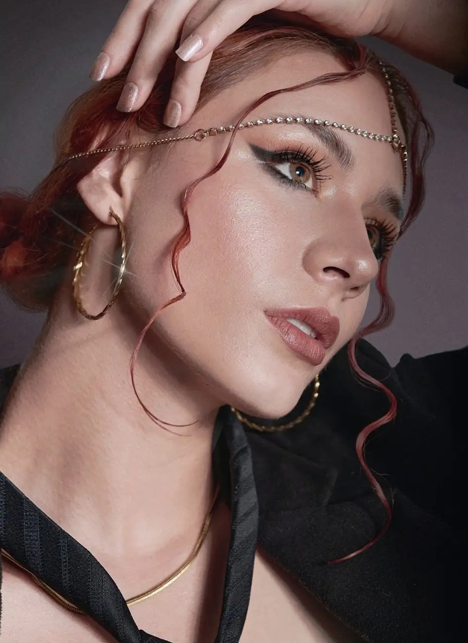 Fotografía beauty de una mujer de ojos verdes, pelo de color rojo, candongas doradas y una cadena de oro en su frente