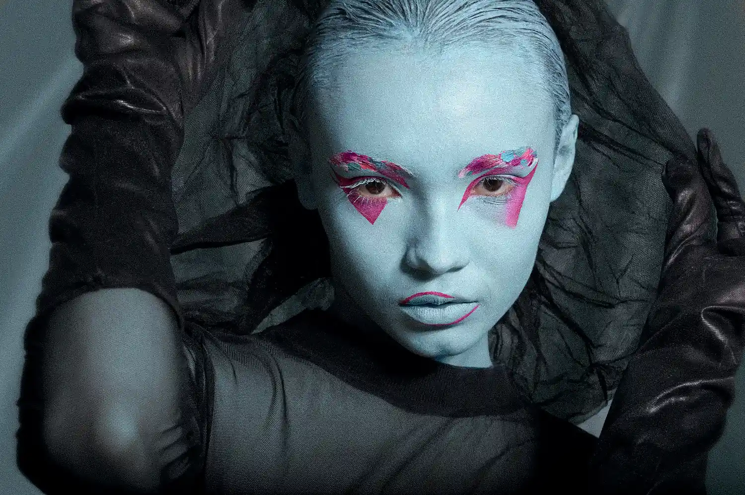 Mujer con maquillaje azul y sombras rosadas, mirando a fijamente a la cámara