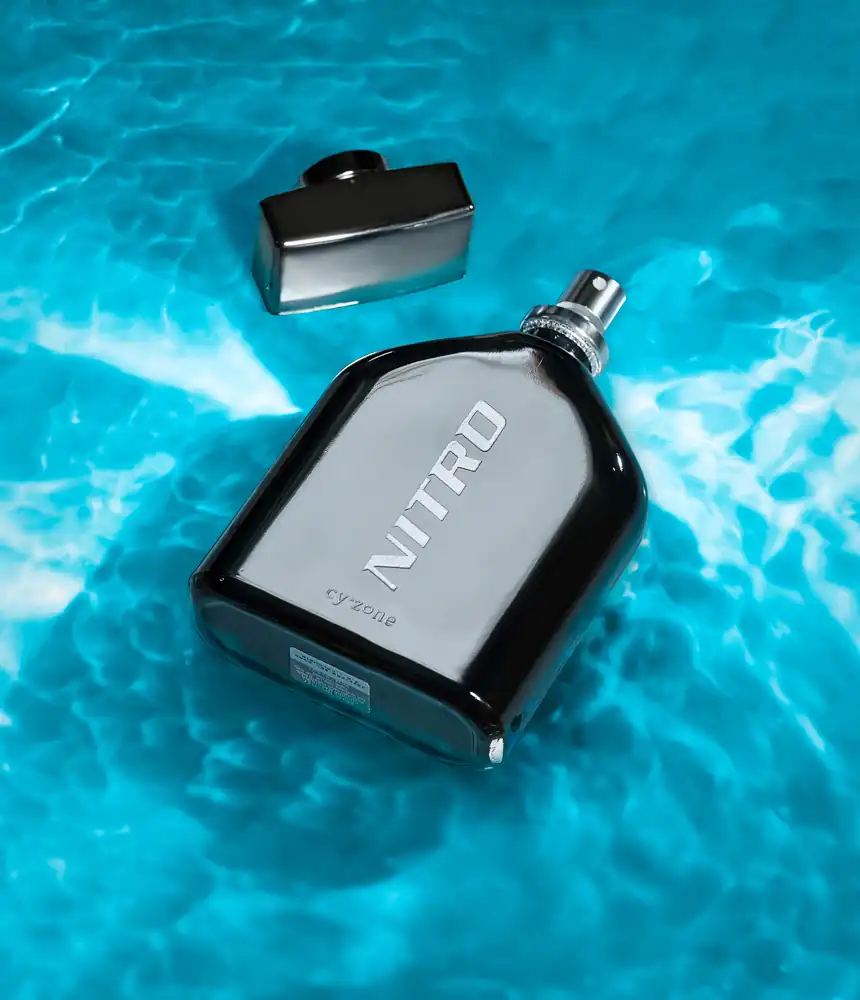 Fotografía de un perfume en agua de color azul y con la tapa a un lado